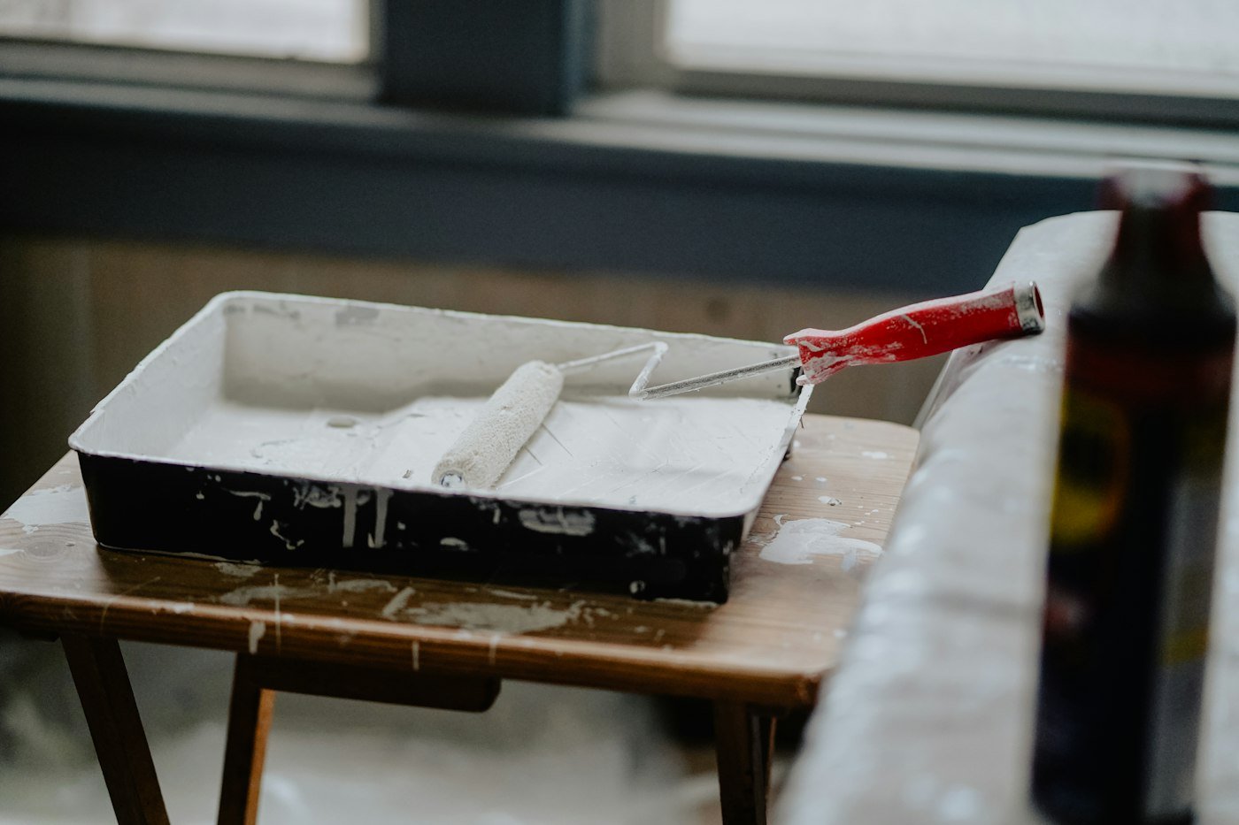 Paint roller resting in a tray of white paint